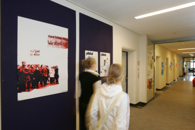 Two people walk past a wall newspaper in a hallway of the university.