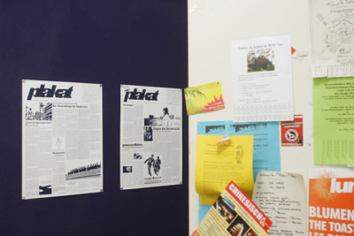 Two wall newspapers hang next to a packed bulletin board displaying student ads.