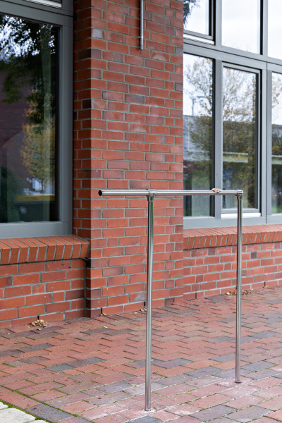 Drei schmale Metallstangen bilden eine Art Geländer. Diese Installation steht auf dem Fußweg, vor den Fenstern des Kunstraum.